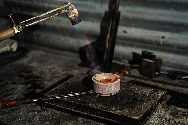 Jeweler manually melting gold using gas torch in crucible
