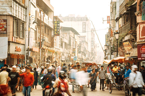 A crowded market street in Varanasi, India, with pedestrians, rickshaws, bicycles, and stalls lining narrow shops under warm light, capturing everyday city life and bustling commerce.