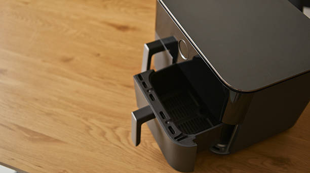 A sleek, black air fryer sits on a warm, polished wooden surface, its basket partially extended, ready for cooking