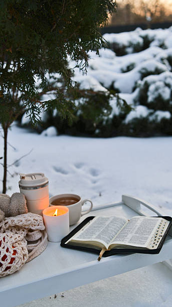 Cozy winter morning with a warm drink, candle, and open book in the snow