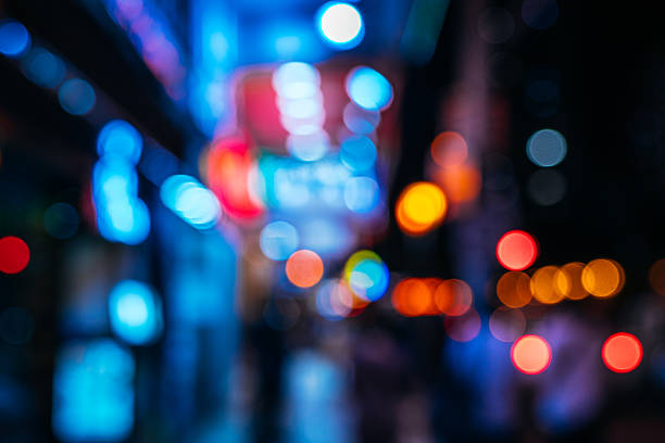 Vibrant neon bokeh fills a Macau street scene at night, with vivid blues, reds, and oranges. Soft silhouettes of people and cars add movement to the urban, nightlife atmosphere.