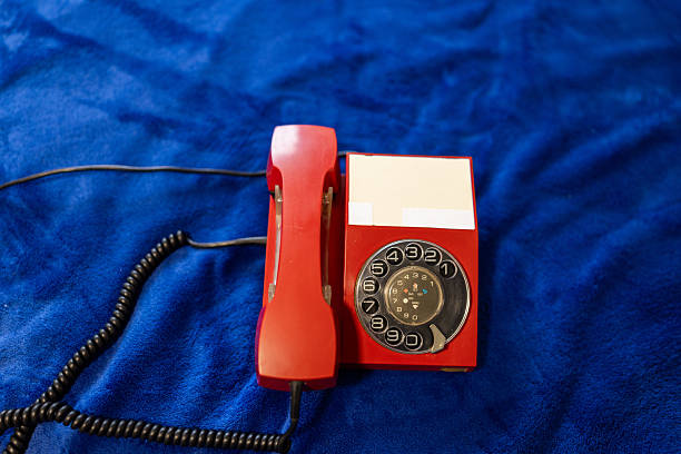 A vintage red rotary phone with a coiled cord rests on a plush blue fabric surface, evoking nostalgia for older communication methods