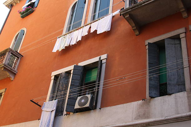 Detail of a traditional Venetian building facade with windows and hanging laundry in Venice, Italy. Strong visual for European lifestyle, architecture, and travel-related content.