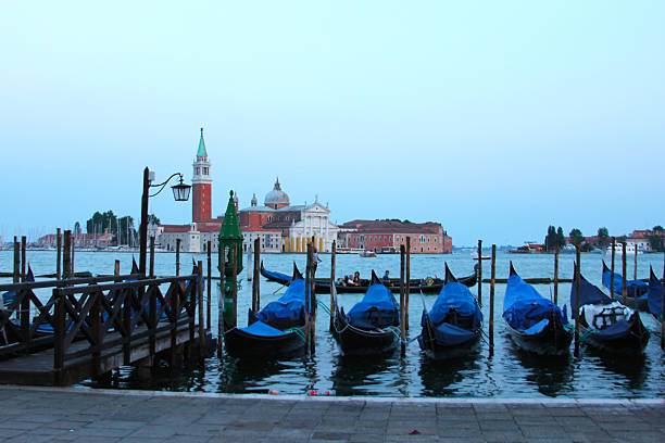 Traditional gondolas moored at a pier in the Venice lagoon, Italy, with historic city skyline in the background. Iconic Venetian scene ideal for travel, tourism, and romantic destination imagery.