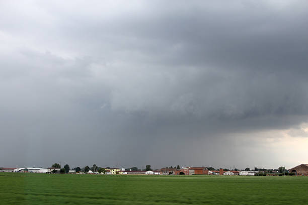 Dark storm clouds and heavy rain falling over flat agricultural fields near a rural settlement. Dramatic weather landscape in the European countryside.