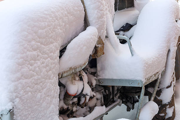 Old agricultural tractor is completely covered with a thick layer of fresh fluffy snow after a heavy winter blizzard. Frozen engine parts and massive wheels of machinery demonstrate the severity of cold season and forced stop.