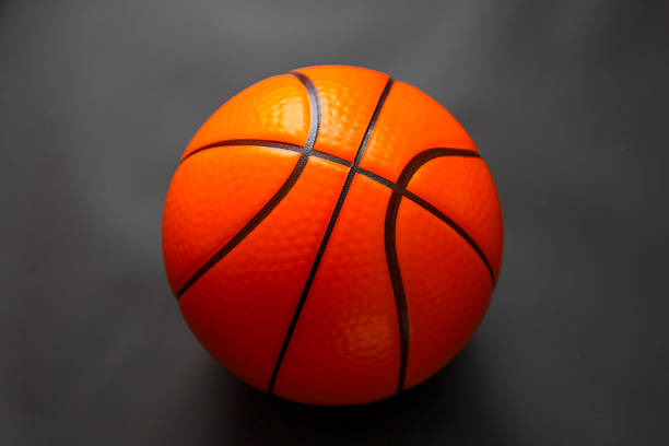 A bright orange basketball with a characteristic textured surface and black stripes is centered against a deep dark background.