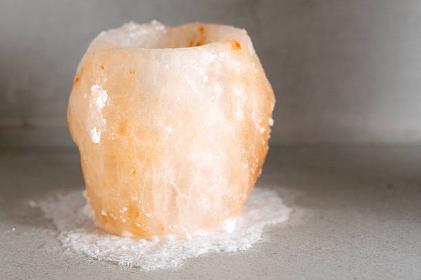 Himalayan salt candle holder on table soft amber glow, coarse crystals scattered, melted wax pool, muted gray background, studio light emphasizing translucent
