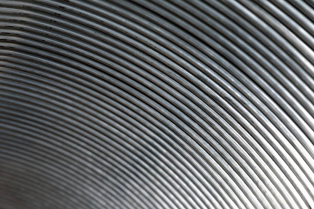 Close up view of tightly wound steel wire forming a repeating curved pattern, creating an abstract industrial texture suitable for manufacturing, construction, engineering and material industry concepts, with detailed metallic surface and copy space