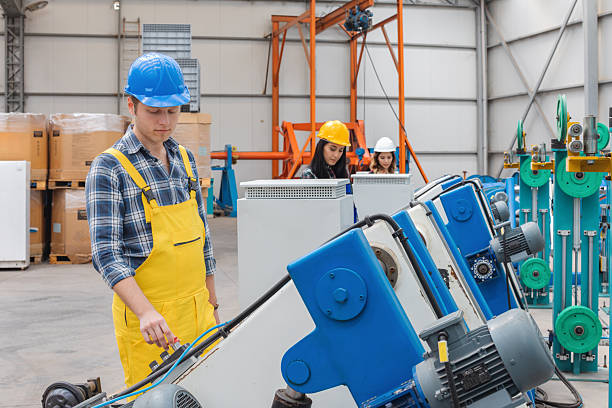 Professional industrial workers wearing safety helmets and protective workwear operate and monitor heavy cable production machinery inside a modern manufacturing factory, showing teamwork, precision engineering, industrial automation and workplace safety in a clean industrial environment