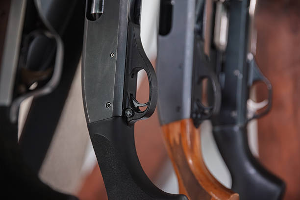 Several shotguns hanging on a rack, showing their triggers and barrels up close