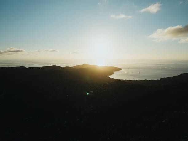 Golden sun lights a tranquil tropical bay off Mahe, Seychelles, casting warm reflections on calm water and silhouetting lush dark hills for a serene coastal vista