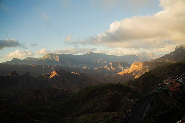 Panoramic sunset view of a mountain valley with clouds and warm evening light. Expansive landscape with depth and texture.