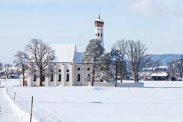 A beautiful old St. Coloman's church and snow covered trees in a winter scenery under blue sky in Schwangau, Allgau, Bavaria, Germany.