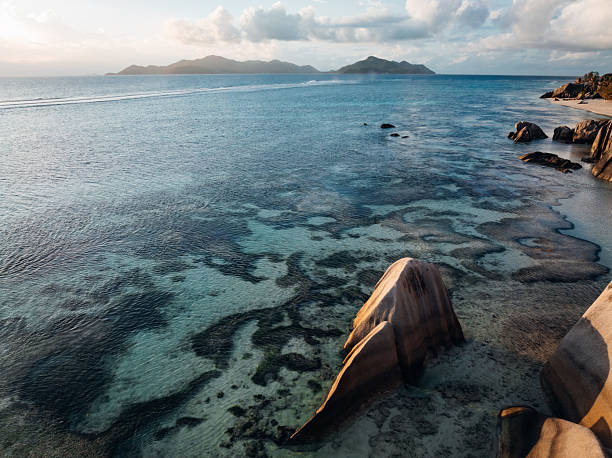 Anse Source d'Argent beach on La Digue island showcasing unique weathered granite rock formations, lush tropical vegetation, and tranquil clear turquoise water of the Indian Ocean at sunset
