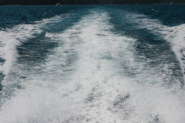 Boat cutting through turquoise ocean, leaving a foamy white wake toward a distant island and small vessel under a bright, clear sky — tropical seascape, motion and freedom