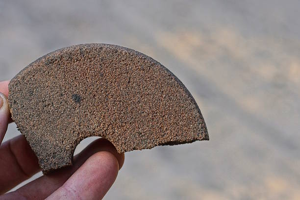 hand holding one piece of gray brown broken stone grinding wheel on the street