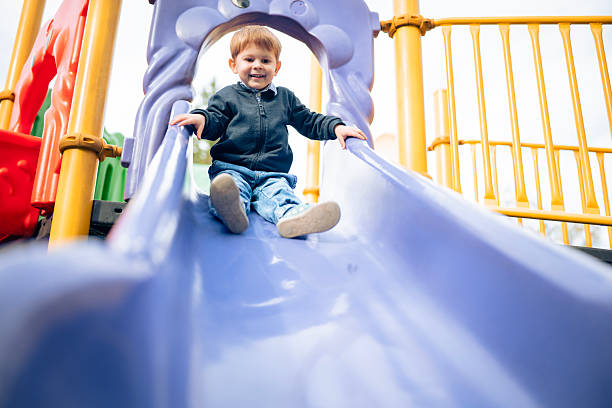 Shot of charming little blonde boy playing on a slide in a public playground.
