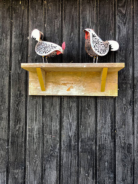 Two cute decorative metal chickens on a shelf in front of a rustic barn wall