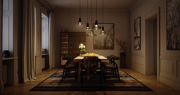 Digitally generated modern dining room interior at night lit by warm pendant lights over a wooden table with black chairs. The striped rug, glass cabinet and framed tree photographs are softly illuminated against darker walls and windows, creating a cozy, intimate atmosphere. Concept for home entertaining, hygge, family gatherings and relaxed dinner parties.