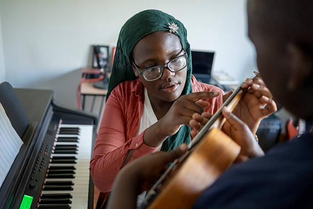 Teenager sister teaching elementary age brother to play ukulele string instrument