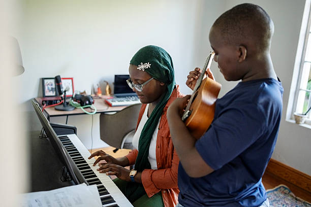 Two siblings playing ukulele and piano together at home