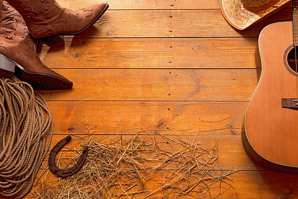 Acoustic guitar, rope, old rusty horseshoe, cowboy hat and boots on a barn wood texture background with some hay. American Country music concept. Space for copy.
