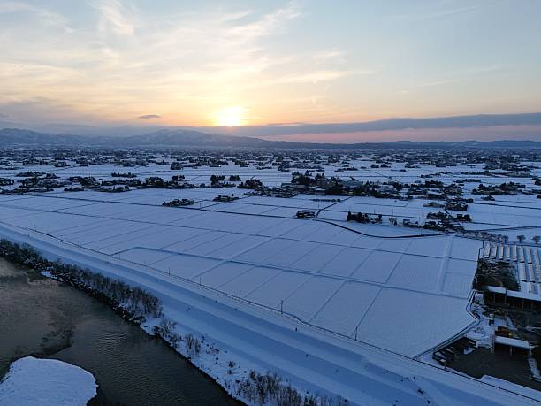 A snowy landscape with a beautiful sunset in the background. The sky is filled with clouds, and the sun is setting, casting a warm glow over the scene