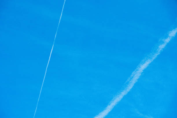 Beautiful white vapor trails from airplanes forming a cross pattern against a vibrant, cloudless blue sky, symbolizing travel, aviation, and connectivity in a minimalist composition.
