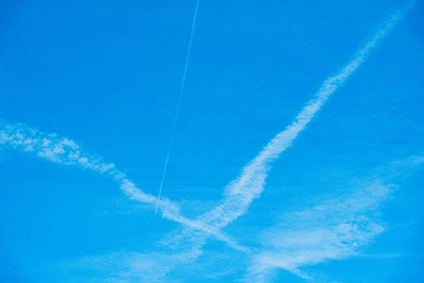 Jet Contrails X Pattern in Sky - Pink sunset light illuminated jet contrails in blue-violet sky.