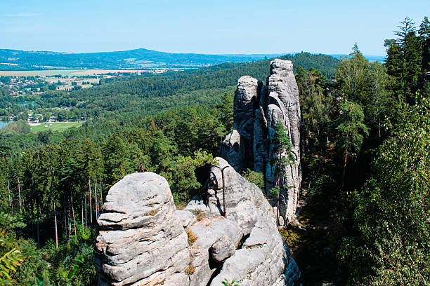 An awe-inspiring summer panorama of the iconic Prachov Rocks sandstone formations in Cesky Raj rising above a lush pine forest under a clear blue sky, featuring ancient stone steps and rugged geological textures.