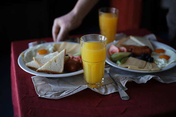 A hearty protein breakfast. A breakfast of eggs, cheese, sausage, and vegetables is laid out on the table, and a man is skewering the food with a fork and knife.