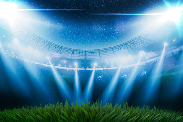 Empty green grass field in a large soccer stadium at night under bright blue spotlights. Blurred arena background with dramatic lighting, perfect for sports events, matches, and tournament themes.