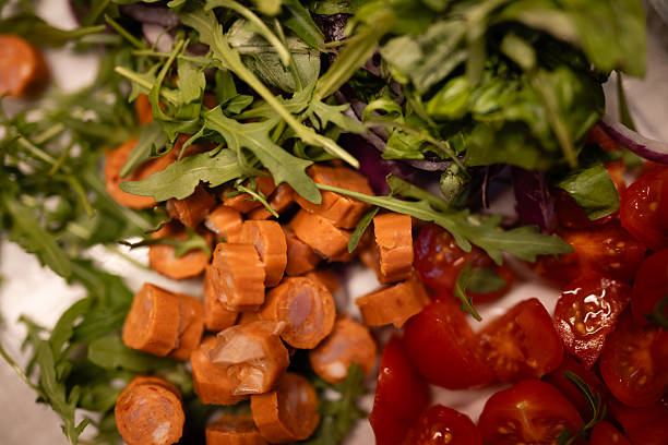 Mixing fresh arugula, chopped cherry tomatoes, red onion, and sliced sausage for a healthy homemade meal preparation