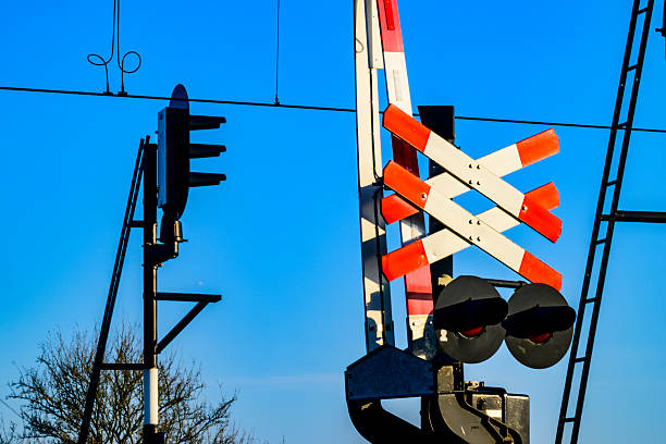 Railway crossing with open barriers and audio visual signals with a blue sky in the background.