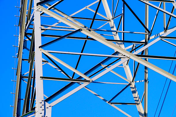 High Voltage electricyty transmission towers with power lines an a blue sky and clouds in the background.