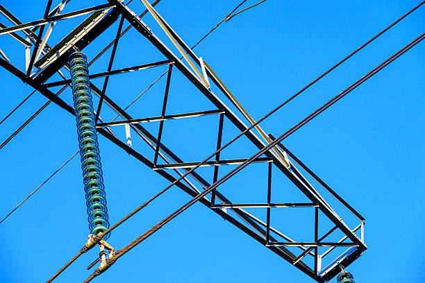 High Voltage electricyty transmission towers with power lines an a blue sky and clouds in the background.