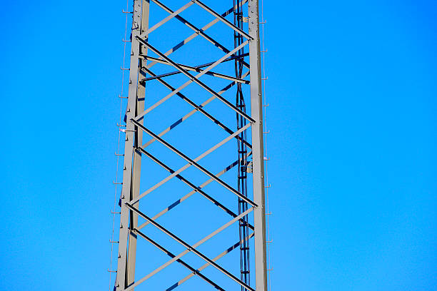 High Voltage electricyty transmission towers with power lines an a blue sky and clouds in the background.