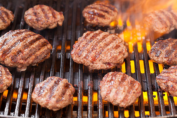 Burger patties cooking on a grill with flames and smoke, outdoor barbecue food preparation scene