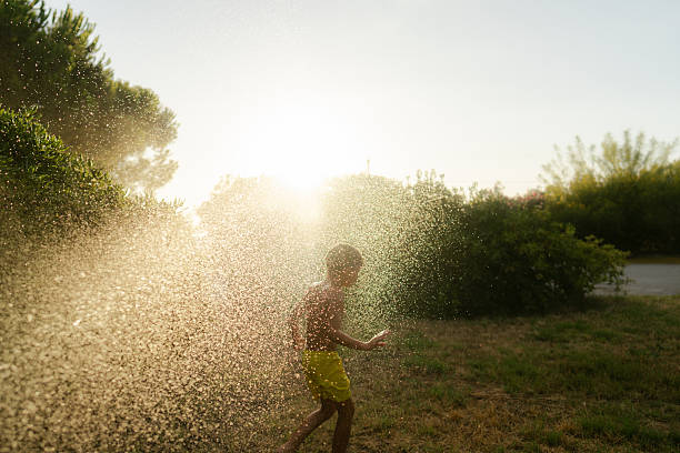 Photo of a young boy jumping over the water sprinkler on a hot summer day in his backyard