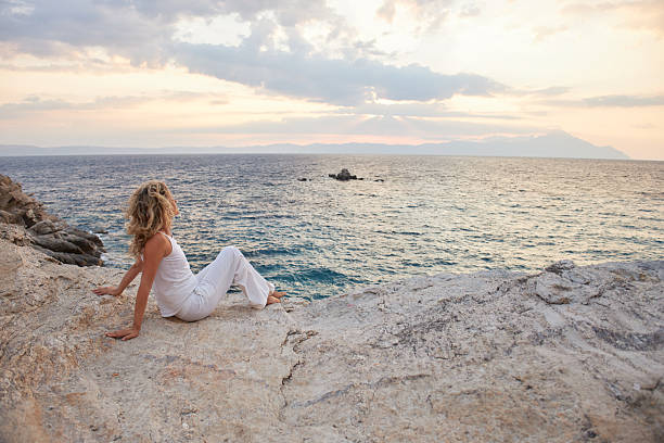 Woman sitting on a rock enjoying the serene ocean view during sunset