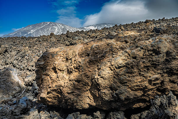 Ancient lava flows dominate the rugged foreground with the majestic, snow-capped Teide volcano rising in the background on Tenerife, Canary Islands, Spain.