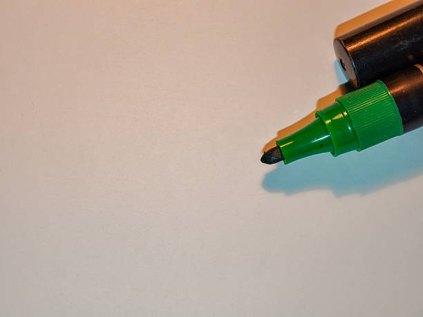 Green marker pen with its cap resting on top, positioned in the upper right corner, showing the felt tip on a checkered transparent background with ample copy space