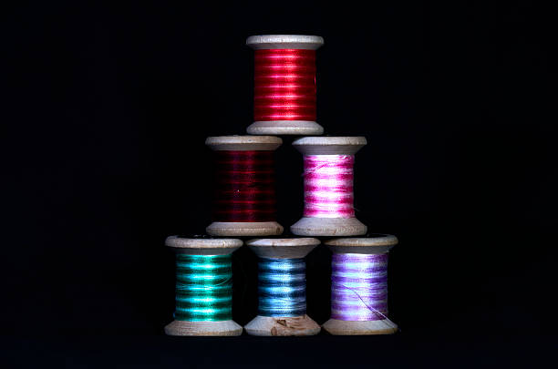 Colorful sewing thread spools stacked in triangle on black background