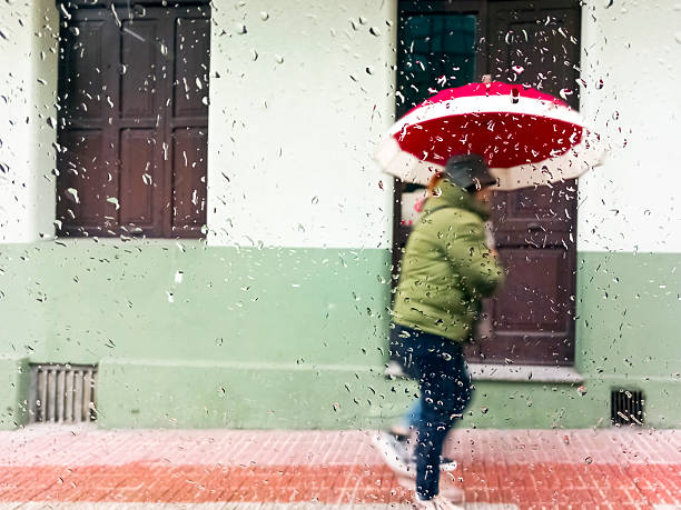 Women walking with umbrella along sidewalk , raindrops on glass. City life in a rainy day. Santiago de Compostela, Galicia, Spain.
