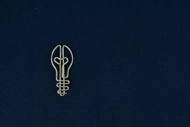 minimal conceptual image of metal paper clip shaped as light bulb symbolizing idea creativity and innovation in business placed on dark blue background with empty space for text commercial design use.