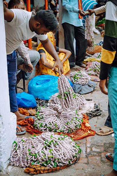 Varanasi, India - November 3, 2024: Bustling street market scene in Varanasi, India, with vendors arranging large jasmine flowers garlands. Colorful fabrics and customers nearby convey commerce, culture, and daily life in a busy Indian market.