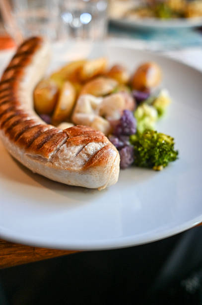 Cooked bratwurst sausage on a white plate with roasted potatoes and colorful vegetables