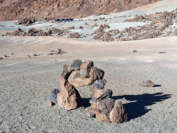 Stacked volcanic rocks forming an arch in a barren desert landscape with mountains