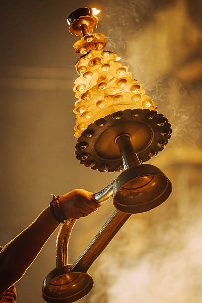 A devout moment in Varanasi as a ceremonial lamp stack is lifted during a fire ritual. Warm, smoky atmosphere, golden glow, and traditional ritual ambiance define this Hindu festival scene.